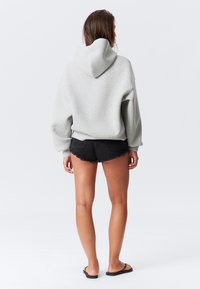 Gray hooded sweatshirt with dropped shoulders, paired with black denim shorts featuring a frayed hem and a casual fit.