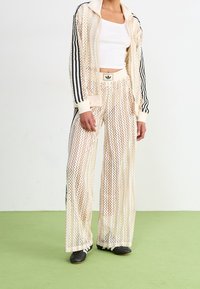 Kevyt, kermaisen värinen verkkoharjoitussuunnitelma mustilla diagonaalisilla raidoilla; sisältää vetoketjuhupparin ja leveälahkeiset housut, joissa on teksturoitu kuvio.