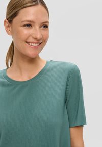 Niebieski, prążkowany t-shirt z okrągłym dekoltem wykonany z gładkiego materiału, z krótkimi rękawami i luźnym krojem, wyeksponowany na jednolitym tle.