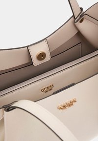 Borsa a mano in pelle beige con hardware dorato, tasca interna con zip e logo in rilievo. Texture liscia con dettagli a contrasto in tonalità scura.