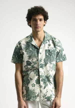 Camisa de manga corta en tela crema con patrones florales tropicales verdes y un bolsillo en el pecho. Presenta un cuello clásico y botones.