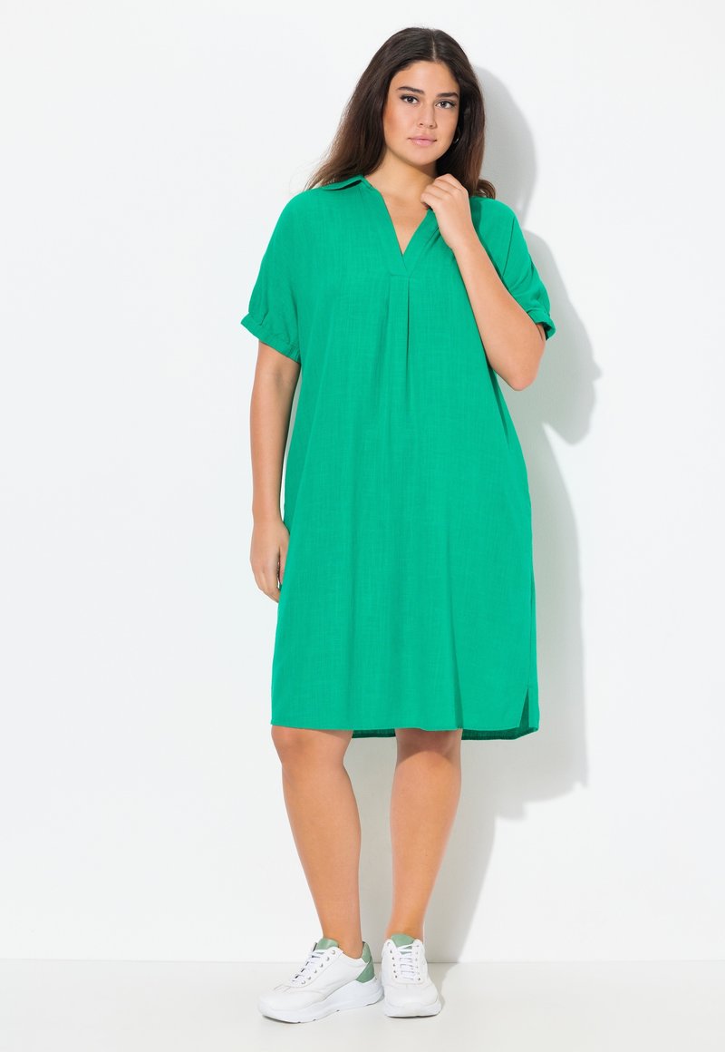 Vestito verde a maniche corte con scollatura a V e dettagli plissettati. Realizzato in tessuto leggero, presenta spacchi laterali. Abbinato a sneakers bianche.