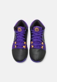 Des baskets noires et violettes avec un dessus texturé, une languette rembourrée, des accents jaunes et une semelle en caoutchouc. Présente des motifs hexagonaux et un système de laçage.