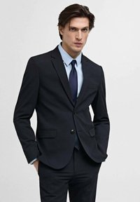 Marineblå jakkesæt med en moderne slim fit, en-knaps lukning, notch revers og to frontlommer. Kombineret med en lyseblå skjorte og en mørk slips.