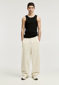 Schwarzes Tanktop, cremefarbene weit geschnittene Hose und hellfarbene Sneakers. Glatter Stoff, lässiger Schnitt und entspanntes Design.