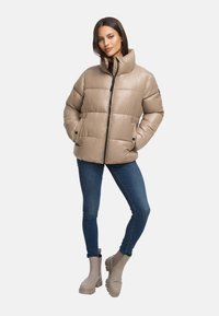 Beige pufferjacka med hög krage, dragkedjestängning och två sidofickor, tillsammans med blå jeans och ljusbeige ankle boots.