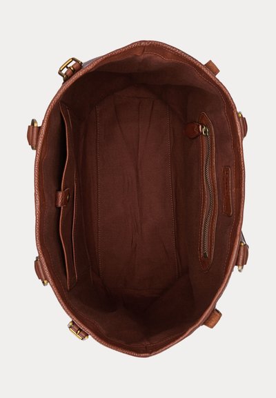 Intérieur d'un sac fourre-tout en cuir marron avec doublure en tissu, une poche zippée à droite et des compartiments ouverts sur le côté gauche.