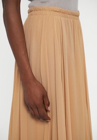 Pleated midi skirt in soft beige fabric with an elastic waistband; smooth texture and flowing silhouette highlighted by gentle draping.