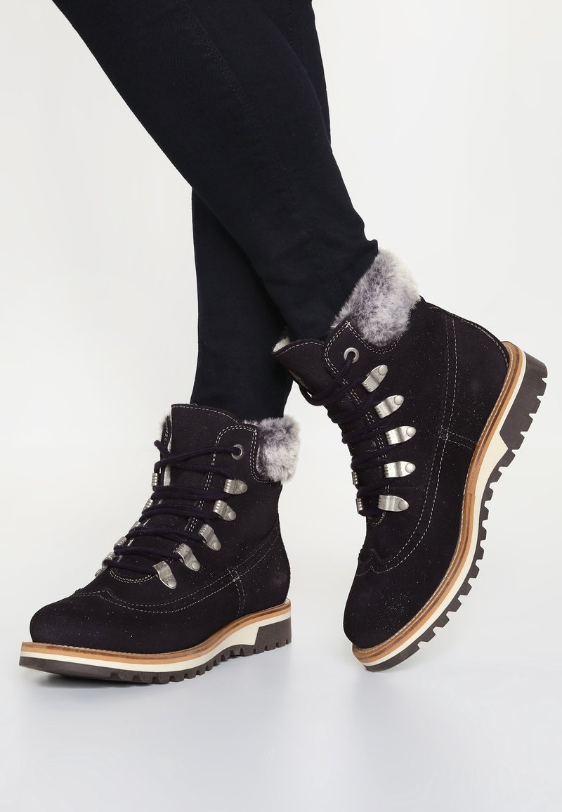 Bottes en daim noir avec un revers en fausse fourrure, des œillets argentés et des lacets. Dotées d'une semelle extérieure en caoutchouc durable et d'une semelle intermédiaire en bois clair.