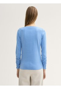 Maglietta azzurro chiaro a maniche lunghe con dettagli arricciati sulle maniche, realizzata in un tessuto morbido, con scollatura rotonda e vestibilità casual.