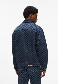 Sötétkék houndstooth mintás farmerdzseki. Hátsó részén márkajelzés található. Klasszikus gallér és gombos mandzsetta.