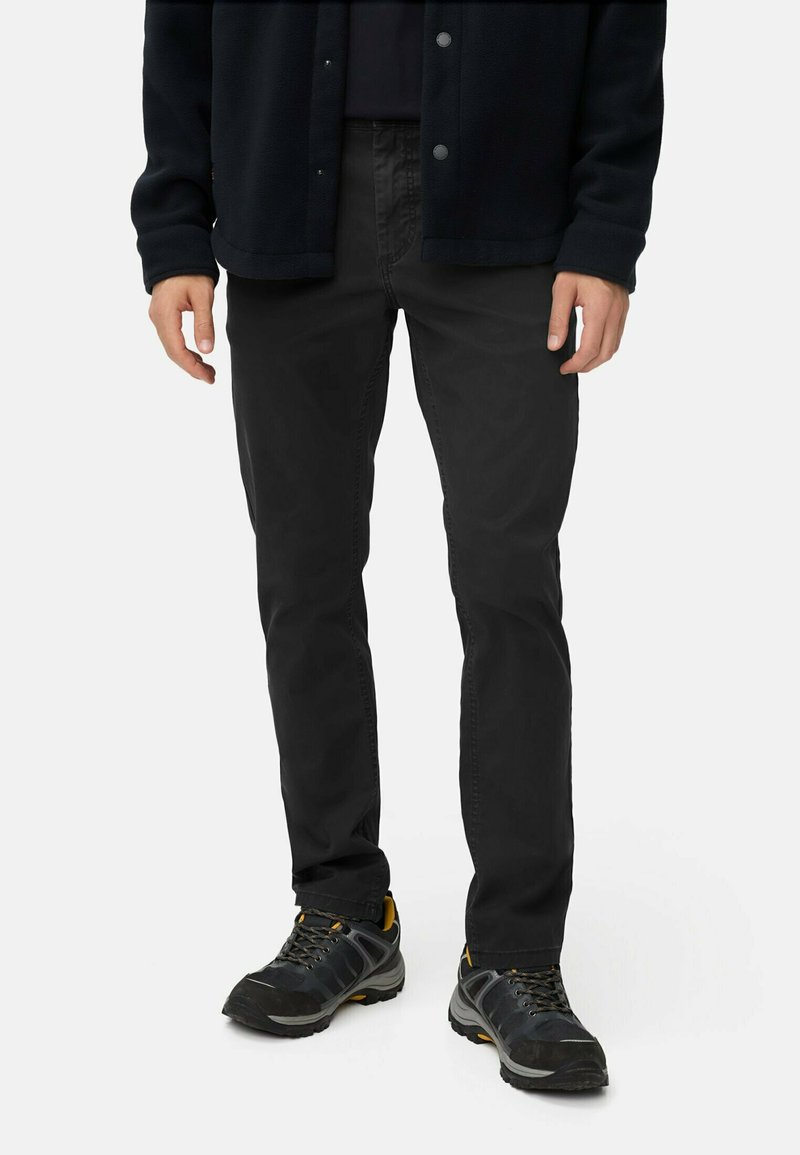 Sorte bukser i slim fit, lavet af slidstærkt stof. Båret med en mørk overdel og robuste sko med gule accenter.