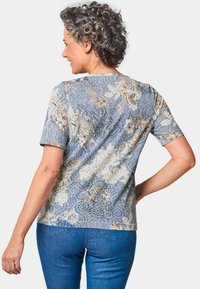 Kurzärmliges blaues Blumenhemd mit detaillierten botanischen Mustern, aus weichem Stoff und mit lässiger Passform. Die Rückansicht zeigt einen abgerundeten Halsausschnitt.