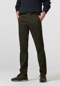 Olijf groene chinos met een slim fit, gemaakt van lichtgewicht katoen, met zijzakken en een gladde textuur, gecombineerd met donkere schoenen.