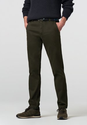 Olivgrüne Chinos mit slim Fit, aus leichtem Baumwollstoff, ausgestattet mit seitlichen Taschen und einer glatten Textur, kombiniert mit dunklen Schuhen.