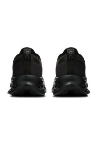 Par de zapatillas deportivas negras con suelas texturizadas vistas desde la parte posterior, mostrando los lazos en el talón y un branding parcial en los lados.