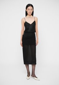 Camisola de cetim preta com alças ajustáveis, sobreposta a uma saia preta franzida com tecido transparente. Modelo usa saltos brancos de bico fino.