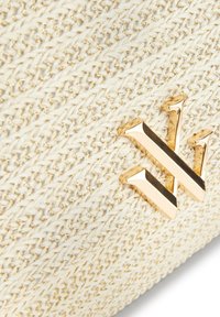 Tessuto a trama intrecciata crema con fili d'oro sottili e un'emblema metallico dorato lucido a forma di "W" attaccato.
