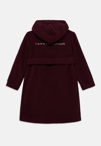 Μπορντό ρόμπα από φλις με κουκούλα, με ζώνη στη μέση και λογότυπο "TOMMY HILFIGER" στην πλάτη. Μαλακή υφή και μακριά μανίκια.