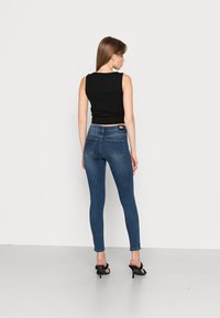 Top preto sem mangas combinado com jeans skinny azul escuro e sandálias de salto alto pretas, exibindo um design justo e uma textura de denim suave.