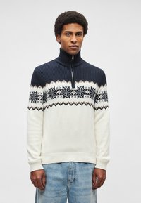 Sweter z golfem, z granatową górną częścią w prążki, kremową dolną częścią oraz wzorem płatków śniegu w kolorze czarnym i beżowym.