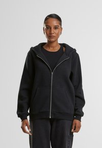 Felpa nera con zip, dotata di un ampio cappuccio, tasche frontali e polsini a coste, realizzata in un tessuto morbido con una superficie liscia.