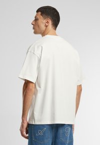 White cotton t-shirt with a relaxed fit, short sleeves, and a crew neckline, paired with blue denim shorts featuring embroidered accents.