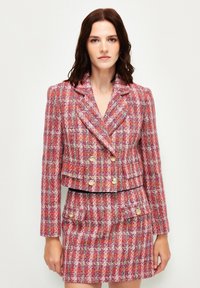 Tweed blazer en rokset in roze, rood en wit met gouden knopen; heeft een dubbelzijdig ontwerp en een gestructureerd patroon.