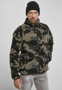 Camouflage fleece jacket in shades of green, gray, and black. Features a high collar, front pockets, and a zip closure. Textured fabric.