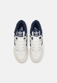 Sneakers in pelle bianca con dettagli blu navy, punta tonda, particolari traforati, chiusura con lacci e suola in gomma. Logo Adidas sulla linguetta e sui lati.