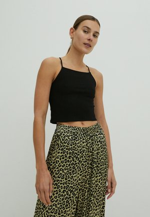 Schwarzes geripptes Crop-Top mit dünnen Trägern, kombiniert mit locker sitzenden, grün-schwarzen Leopardenprint-Hosen. Einfaches Design, weicher Stoff.