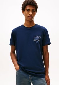 Marineblå bomulls t-skjorte med korte ermer, med en hvit grafisk logo på venstre bryst og en avslappet passform. Brukt sammen med blå jeans.