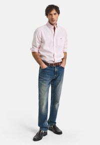 Ljusrosa långärmad skjorta med knappar, blå denim jeans, brun läderbälte och mörkbruna skor med texturfinish.