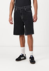 Sorte denim shorts med en afslappet pasform, der har fem lommer, en knaplukning og kontraststing. Båret med sorte sneakers og hvide sokker.