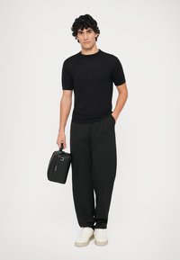 Svart kortermet teksturert topp med et rutemønster, kombinert med løse svarte bukser og hvite sneakers; holder en svart rektangulær veske.