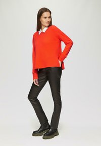 Roter Pullover mit weißen Kragen, kombiniert mit schwarzen, eng anliegenden Hosen und klobigen schwarzen Stiefeln. Glatte Textur, klare Linien und zeitgemäßer Stil.