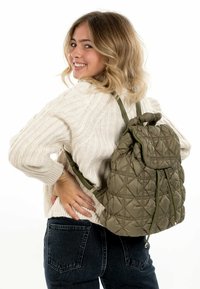 Sac à dos en olive matelassé avec un cordon de serrage et des bretelles réglables. Tissu texturé et doux avec un motif de losanges.
