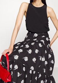 Top negro sin mangas combinado con una falda negra con patrones florales blancos y un dobladillo en volantes, sostenido con un bolso rojo.