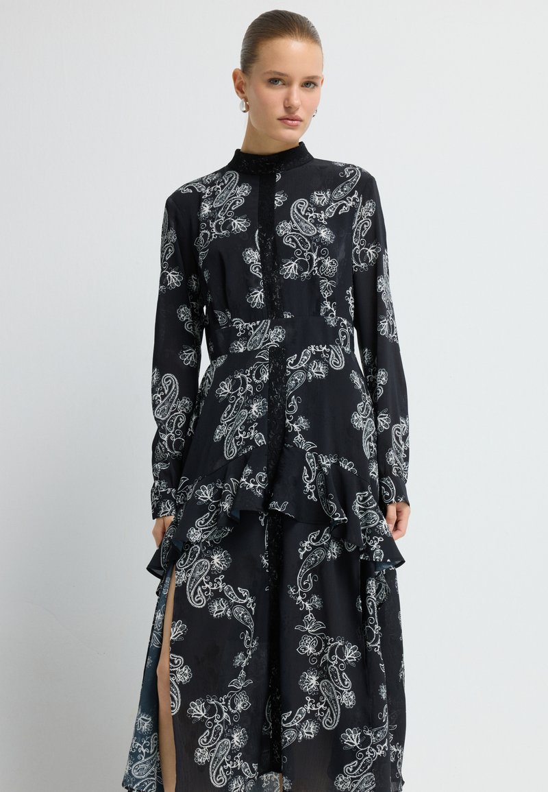 Lang zwarte jurk met een wit paisleyprint, geschulpte zoom, kraag en knoopsluiting voor. Gemaakt van lichte, vloeiende stof.