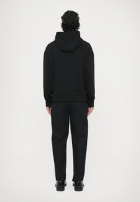 Czarna bluza z kapturem z kieszenią kangurką, ściągaczem u dołu i przy mankietach. Zestawiona z ciemnymi spodniami i czarnymi butami. Prosty, luźny krój.