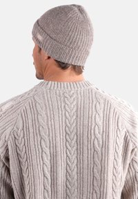 Bonnet en tricot gris avec une texture côtelée ; associé à un gros pull en tricot torsadé d'une nuance de gris similaire, présentant des motifs texturés et un col arrondi.