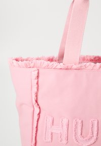 Borsa tote rosa con bordo superiore sfilacciato e dettaglio ricamato "HU". Realizzata in materiale morbido, con manici in tessuto resistenti.