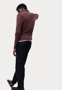 Suéter burdeos de mangas largas, combinado con pantalones oscuros azul marino. El suéter cuenta con un escote redondo y puños acanalados.