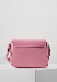 Rosa syntetisk crossover taske med en fold-over flap, gul hardware og justerbar rem. Glat tekstur og rektangulær form.
