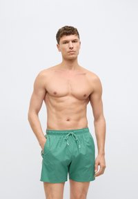 Zelené plavkové šortky s elastickým pásom a sťahovacou šnúrkou, vybavené bočnými vreckami a jednoduchou, hladkou textúrou.