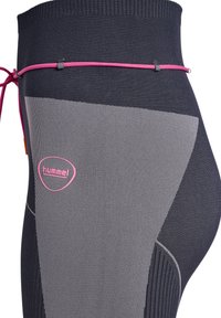 Close-up van donkergrijze en lichtgrijze sportleggings met een roze trekkoord en roze hummel-logo aan de zijkant.