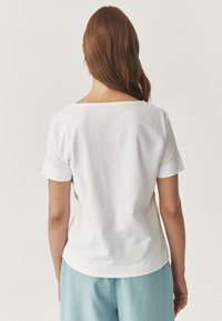 Hvid bomulds t-shirt med bred halsudskæring og korte ærmer, der har en afslappet pasform. Den er parret med lyseblå bukser.