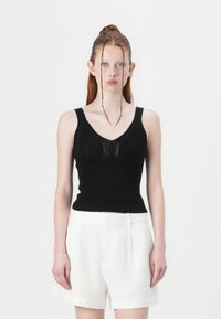 Top din tricot negru, cu un design ajustat, având un decolteu în V și modele texturate. Asortat cu pantaloni scurți din in alba.