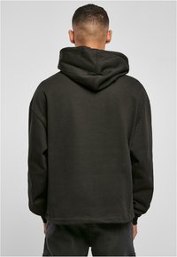Sudadera negra con un corte relajado, que cuenta con una capucha amplia, mangas largas y una textura suave. El dobladillo es recto, combinando con unos jeans oscuros.