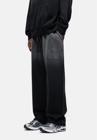Zwarte hoodie met een voorzak, gecombineerd met zwart-grijze gradient joggingsbroek met een logo. Draagt met grijze sportschoenen.